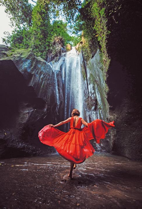 Femme en robe rouge dansant devant une cascade